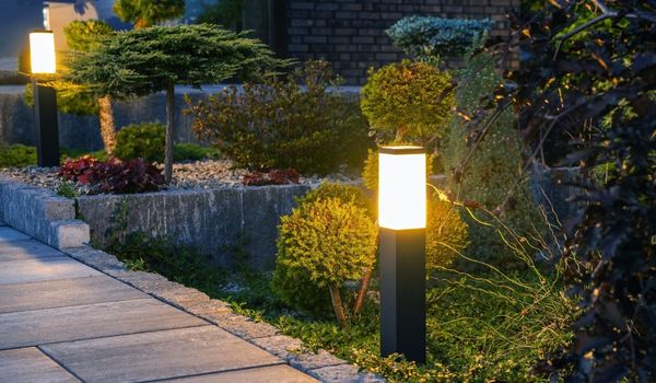 Lit garden path with glowing bollard lights beside manicured shrubs and stone edging