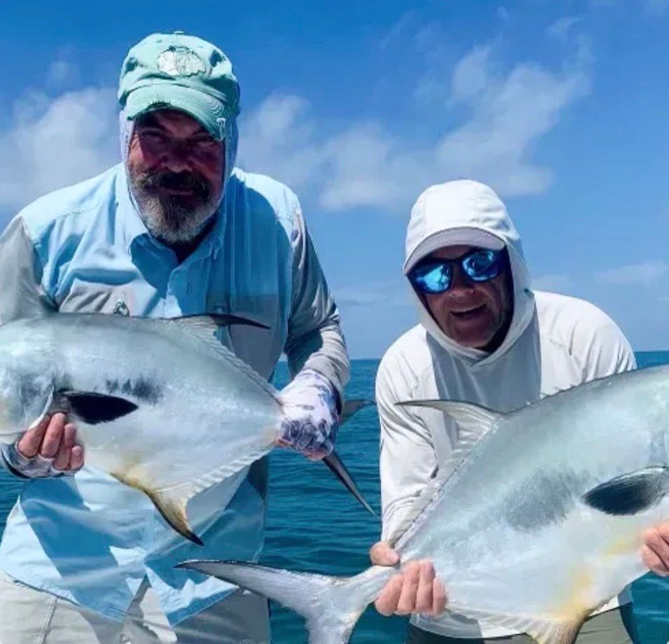 Two men on a boat hold up large fish. Blue water and sky, sunny day. One man has a beard.
