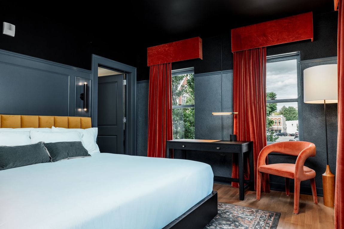 A floating wooden nightstand with a small plant and books sits beside a bed against a vertical, dark brown headboard.