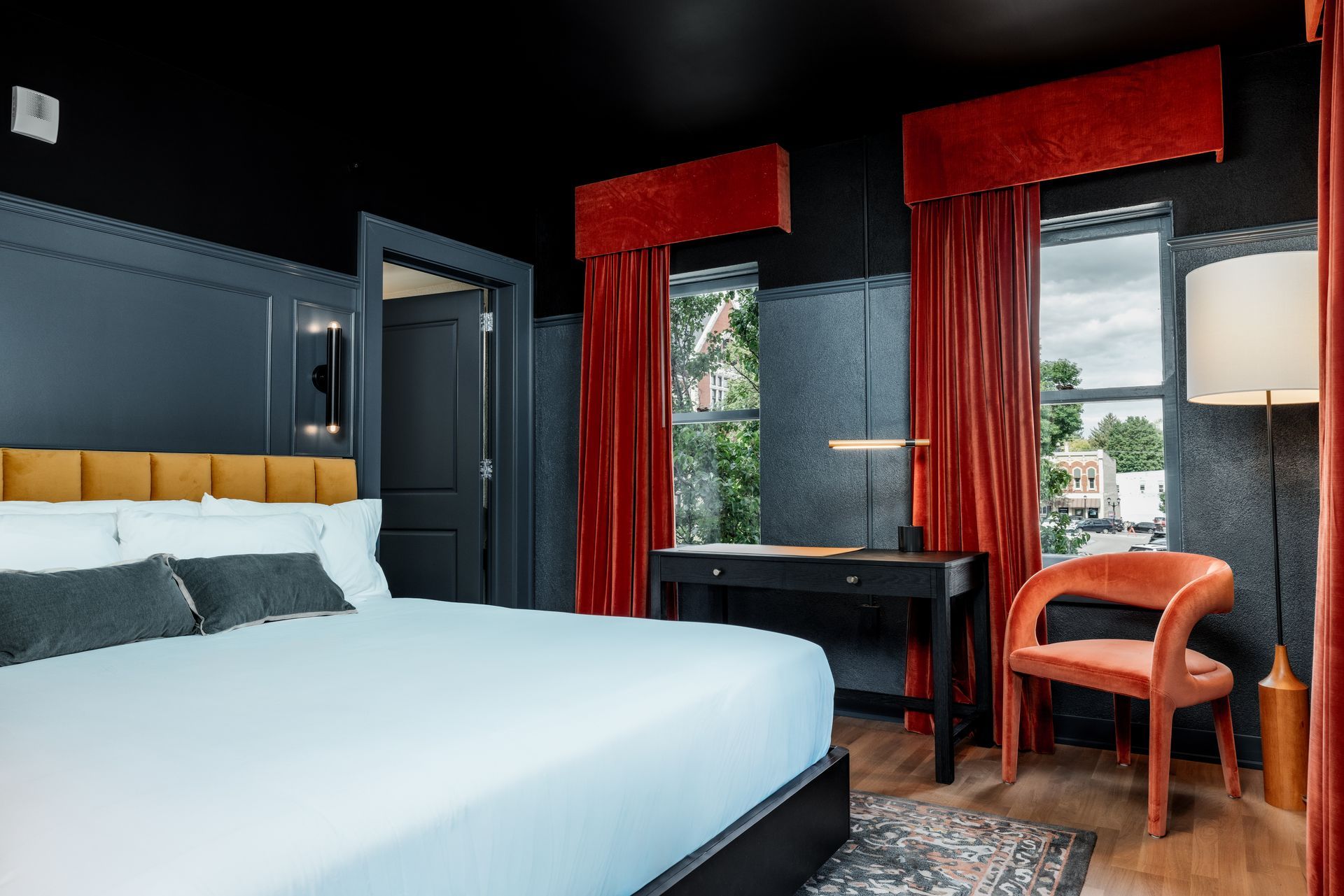A floating wooden nightstand with a small plant and books sits beside a bed against a vertical, dark brown headboard.