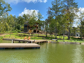 There is a dock in the middle of a lake with a house in the background.