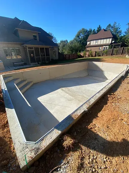 A large concrete pool is being built in the backyard of a house.