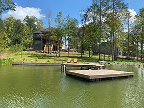 There is a dock in the middle of a lake with a house in the background.
