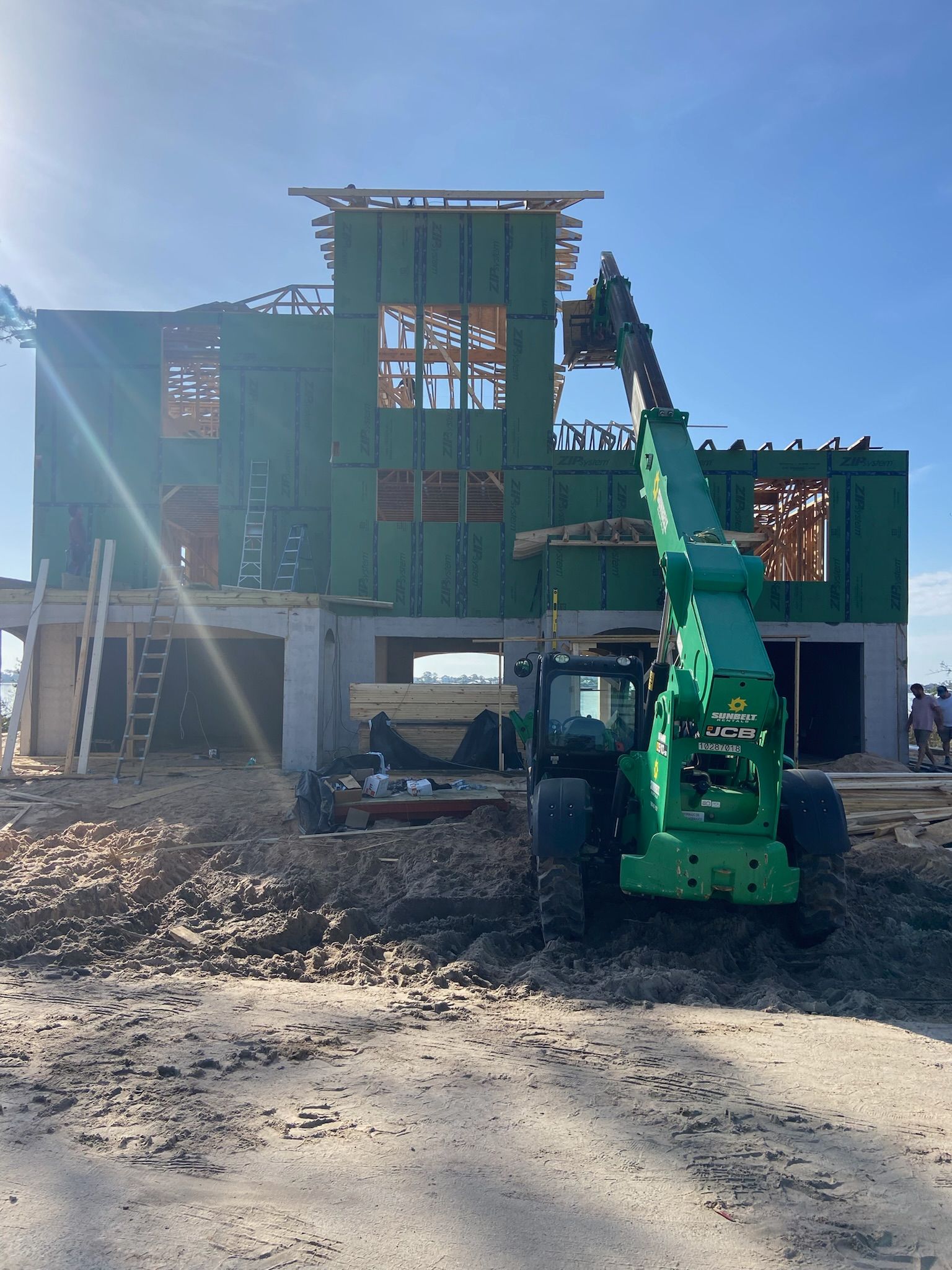A green construction vehicle is parked in front of a house under construction.