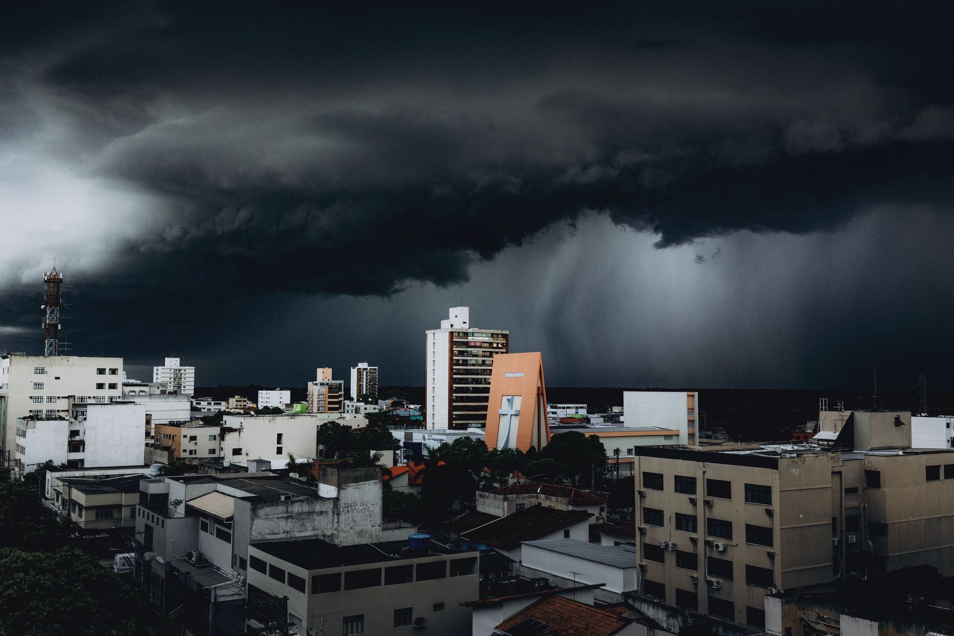 Dark storm clouds over a city skyline with heavy rain in the distance