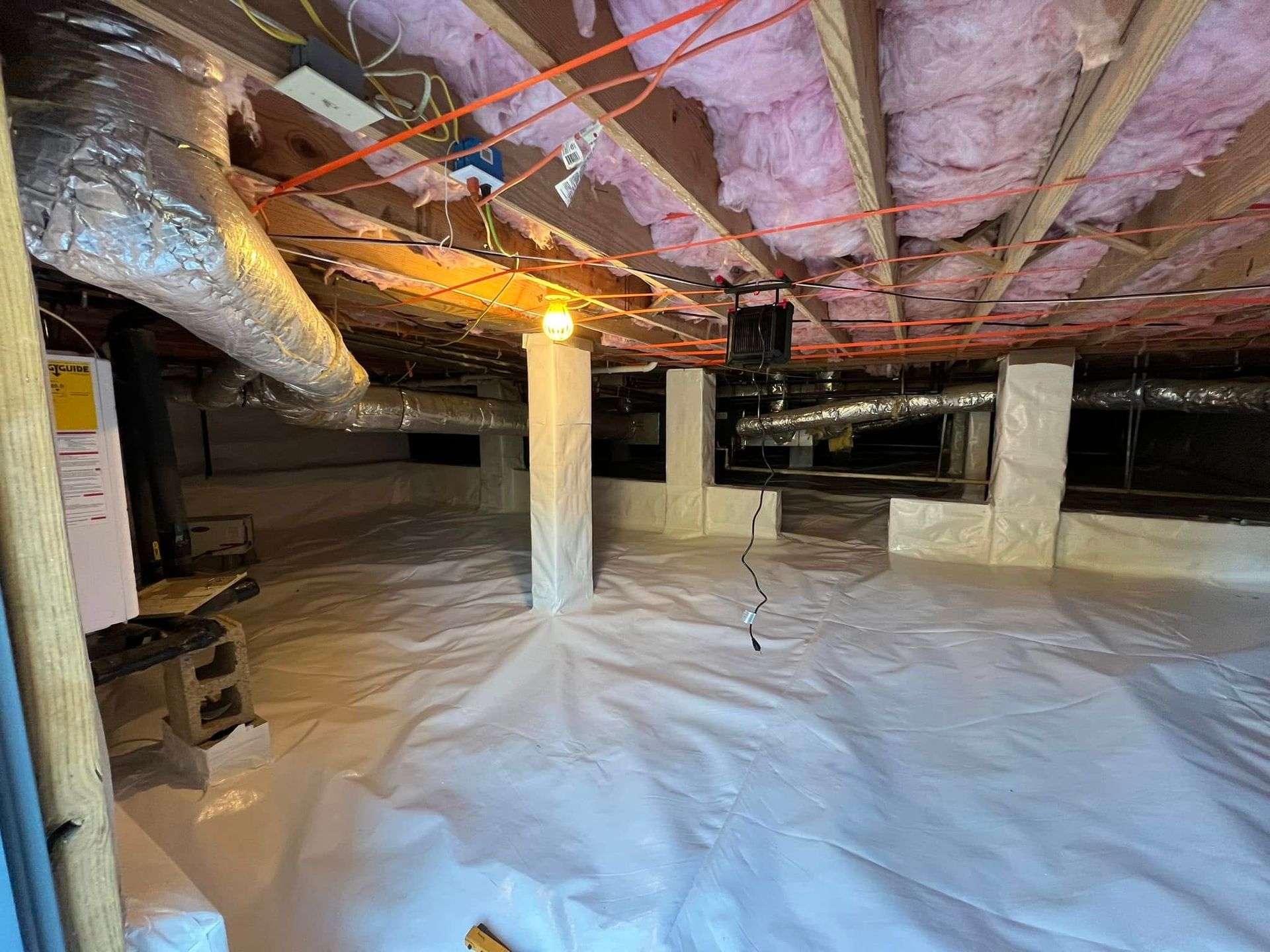 A clean, dry crawl space featuring a white vapor barrier on the ground, wrapped support pillars, and pink ceiling insulation.