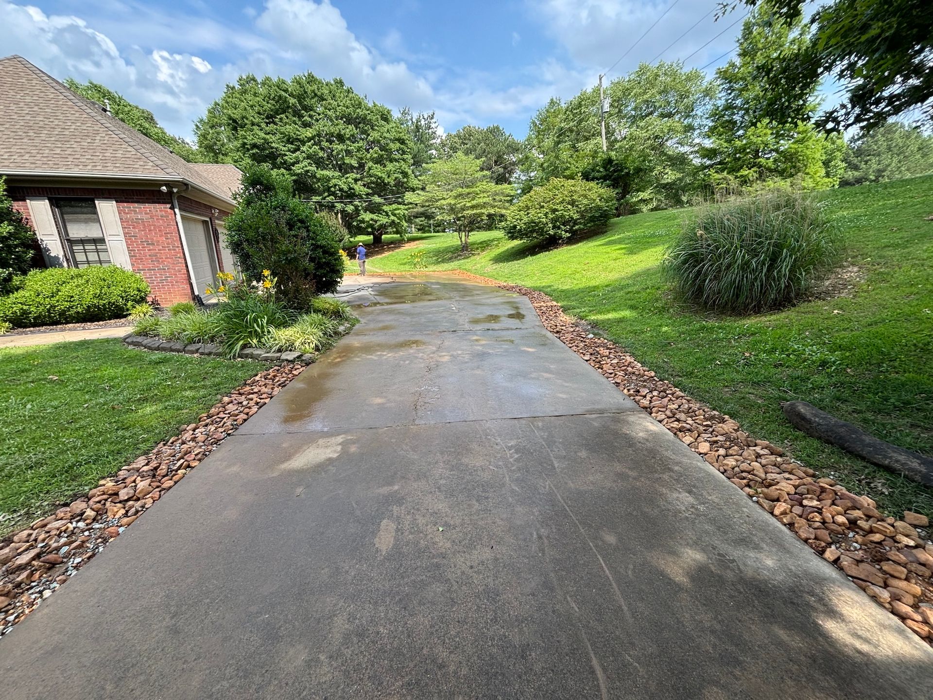 A concrete driveway winds toward a brick house, bordered by gravel and grass on a sunny day.