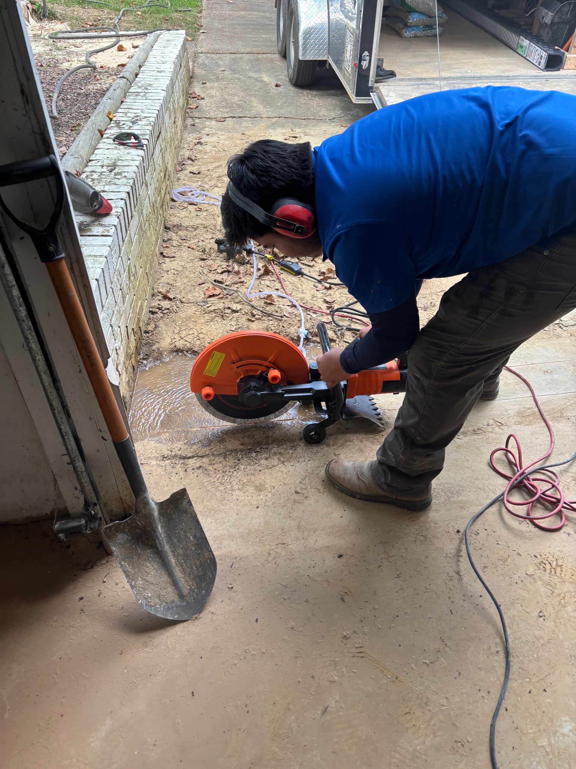 A person in a blue shirt uses an orange handheld circular concrete saw to cut into a concrete surface.