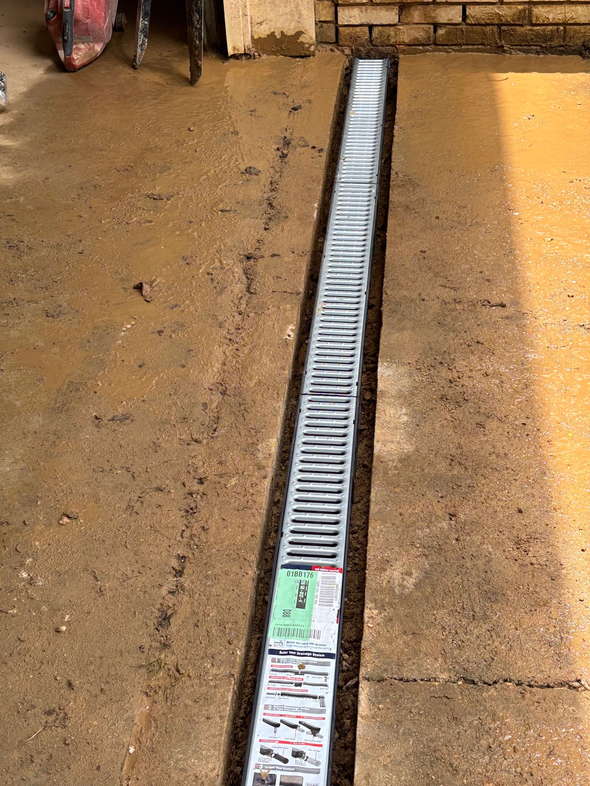 A newly installed trench drain with a silver metal grate set into a concrete path.