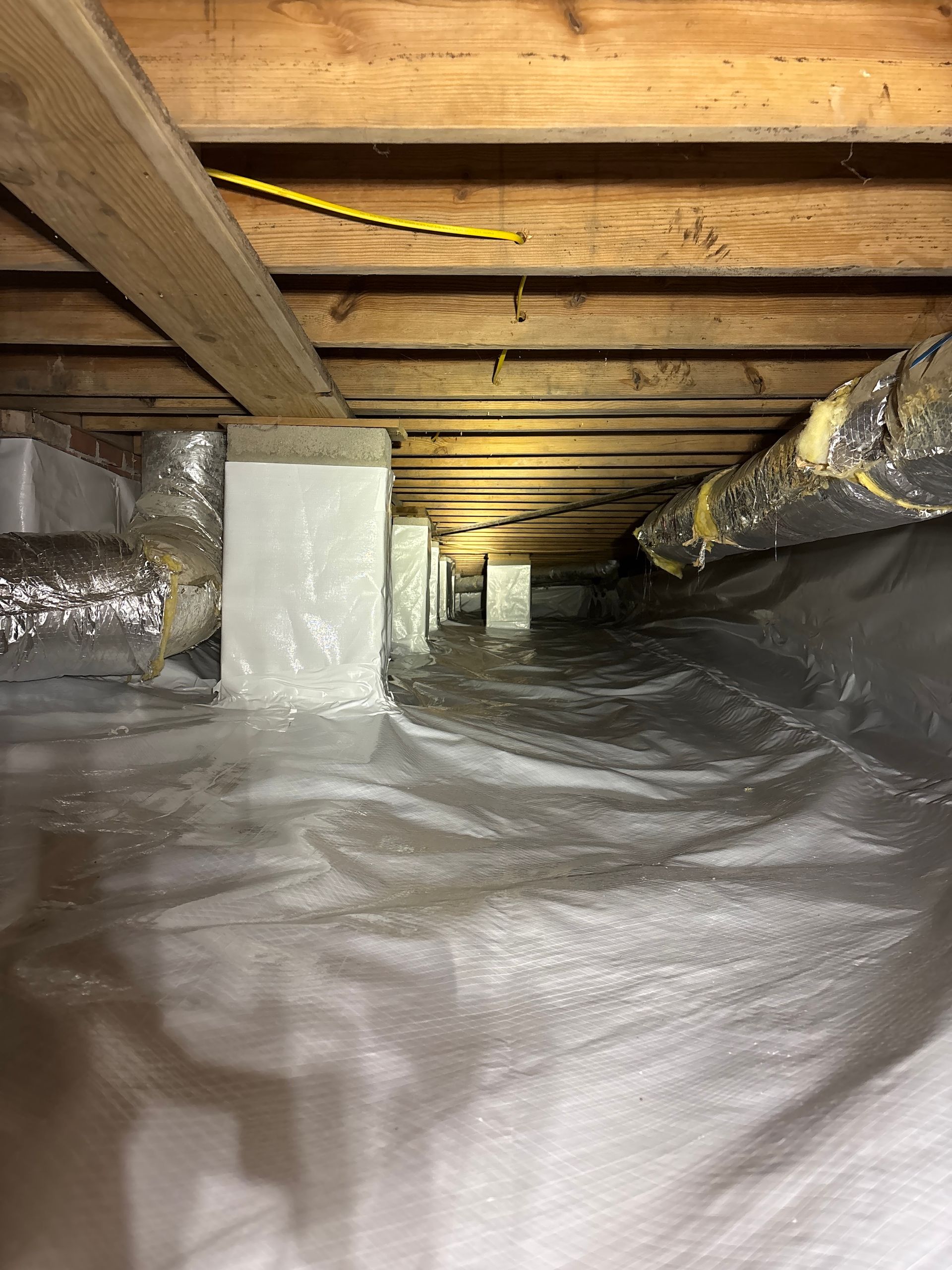 Crawl space interior with white vapor barrier, wooden floor joists, and insulated HVAC ductwork.