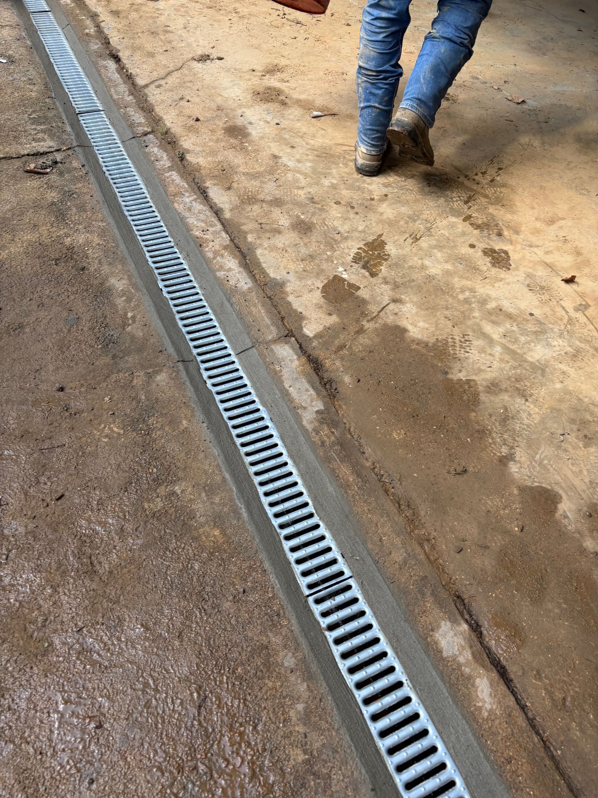 A metal trench drain grate embedded in a concrete floor, with a person walking away in the background.