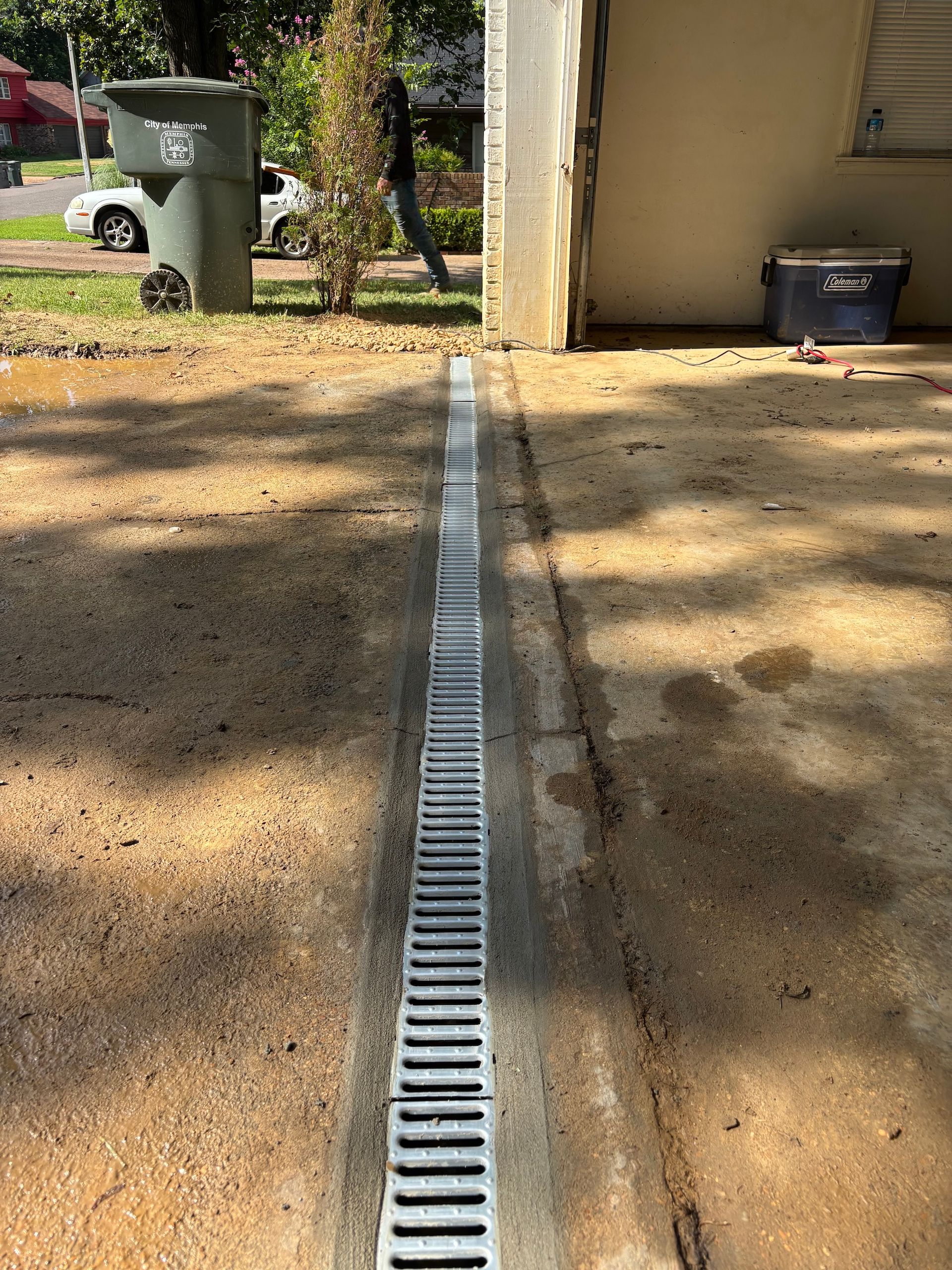 A linear metal trench drain installed in a concrete driveway near a residential garage.