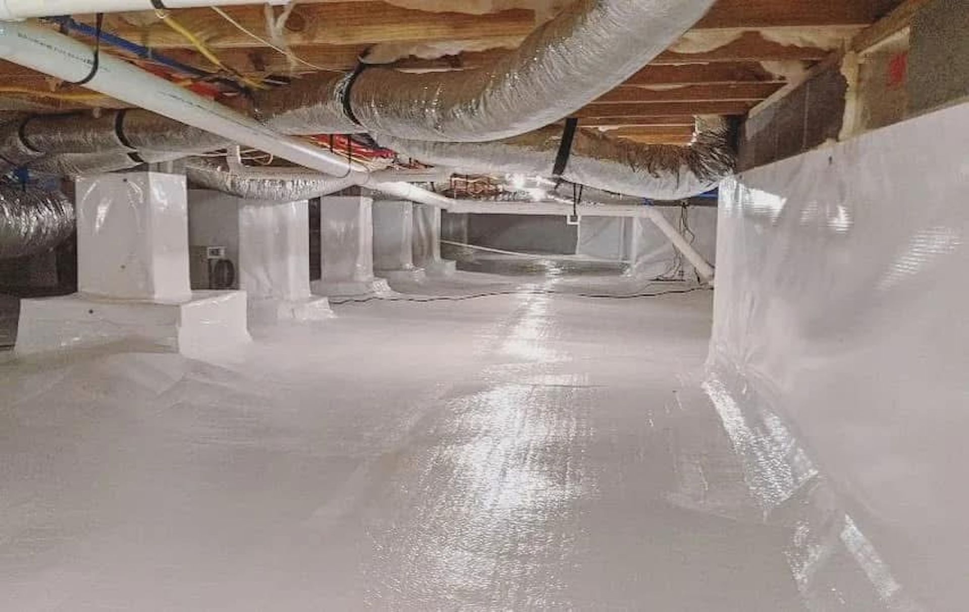 A crawl space encapsulated with white vapor barrier plastic on the floor and walls, with exposed floor joists and ductwork.