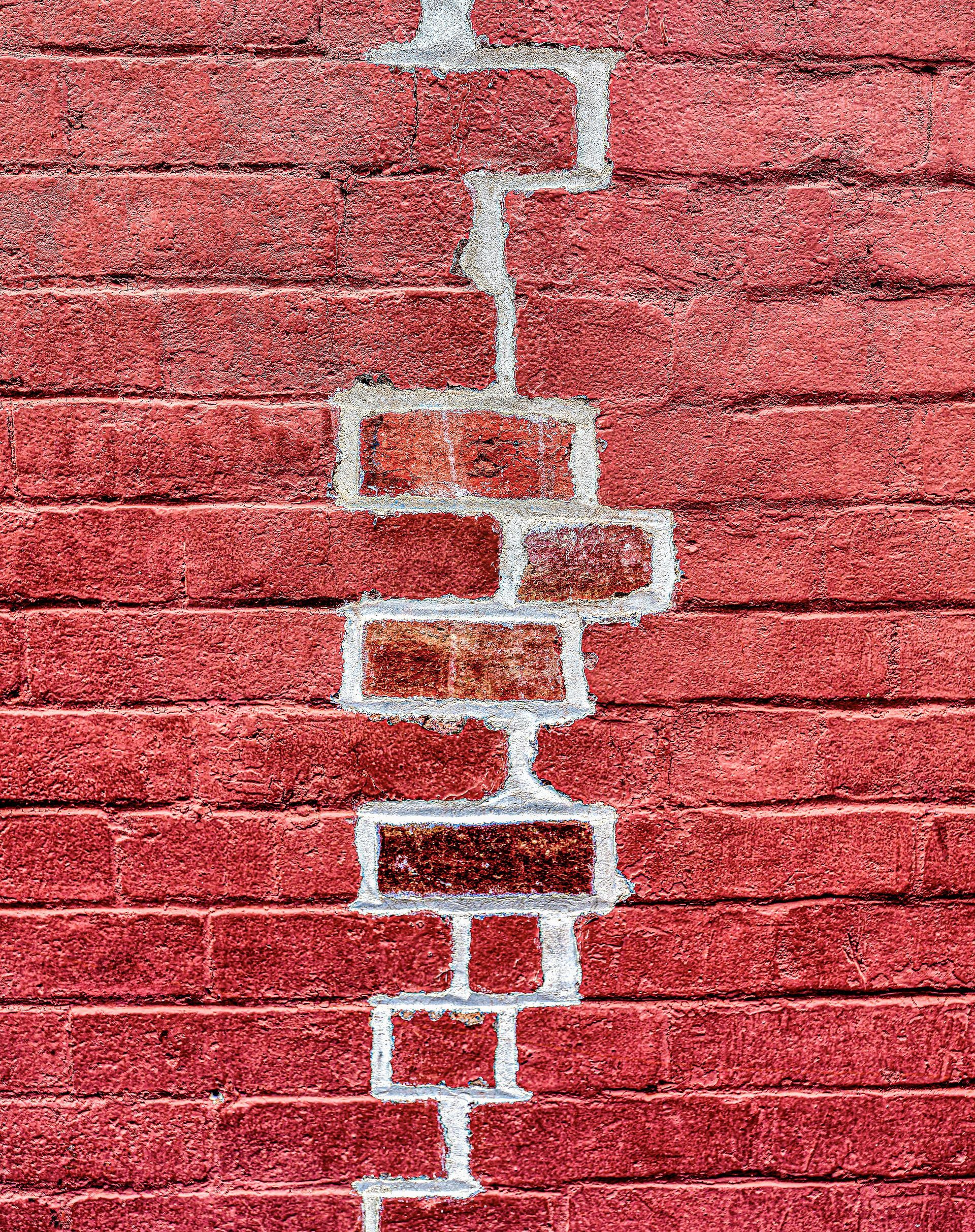 Cracked red brick wall with a vertical zigzag of white mortar repairs