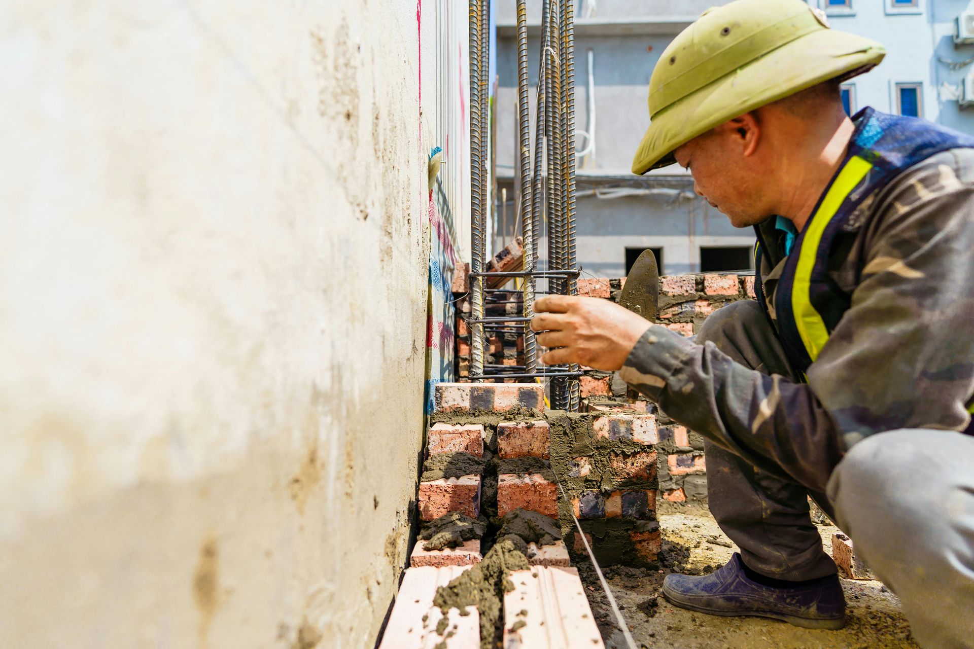 Worker in hard hat inspecting steel rebar at a construction site wall
