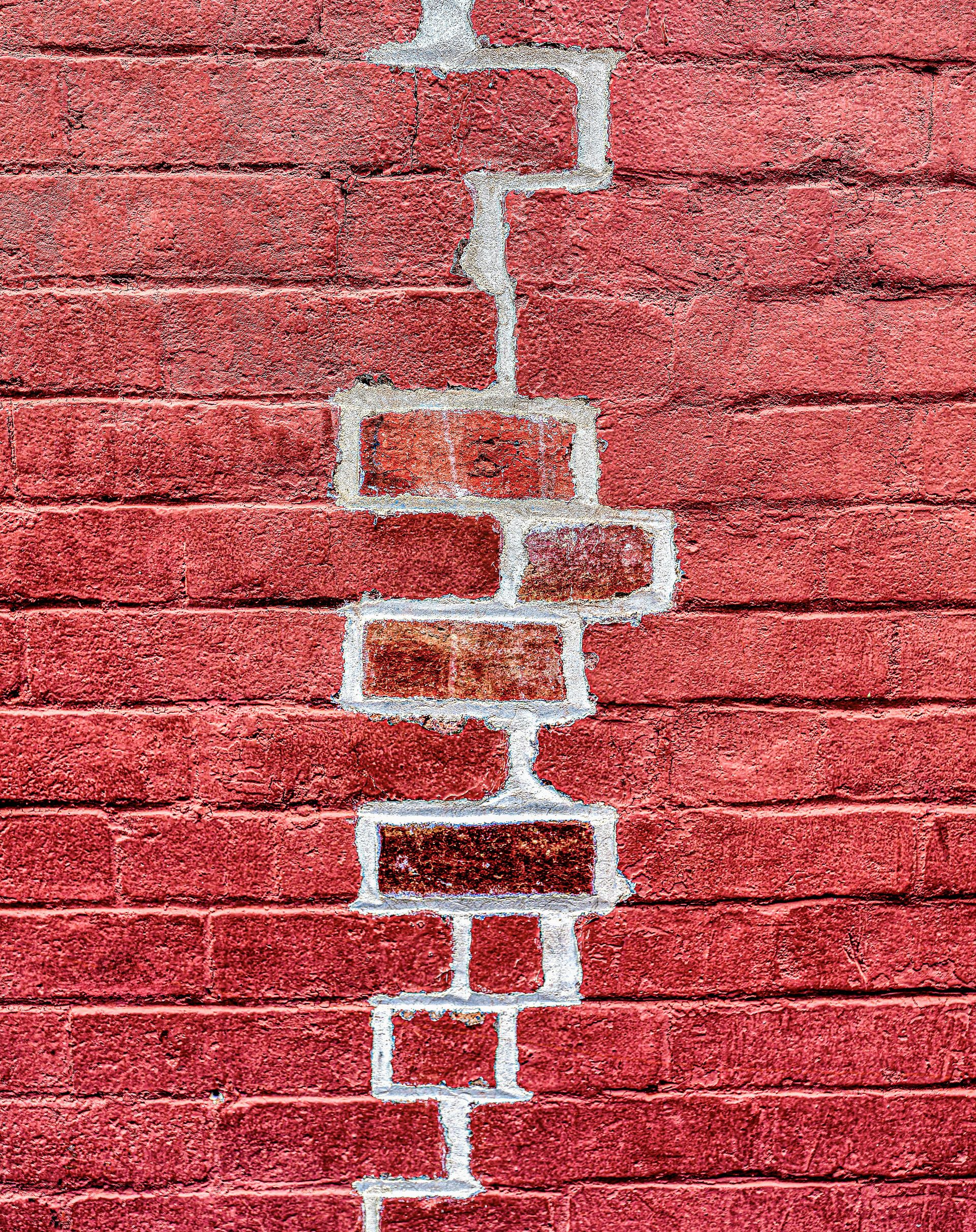 Red brick wall with a vertical white crack zigzagging down the center