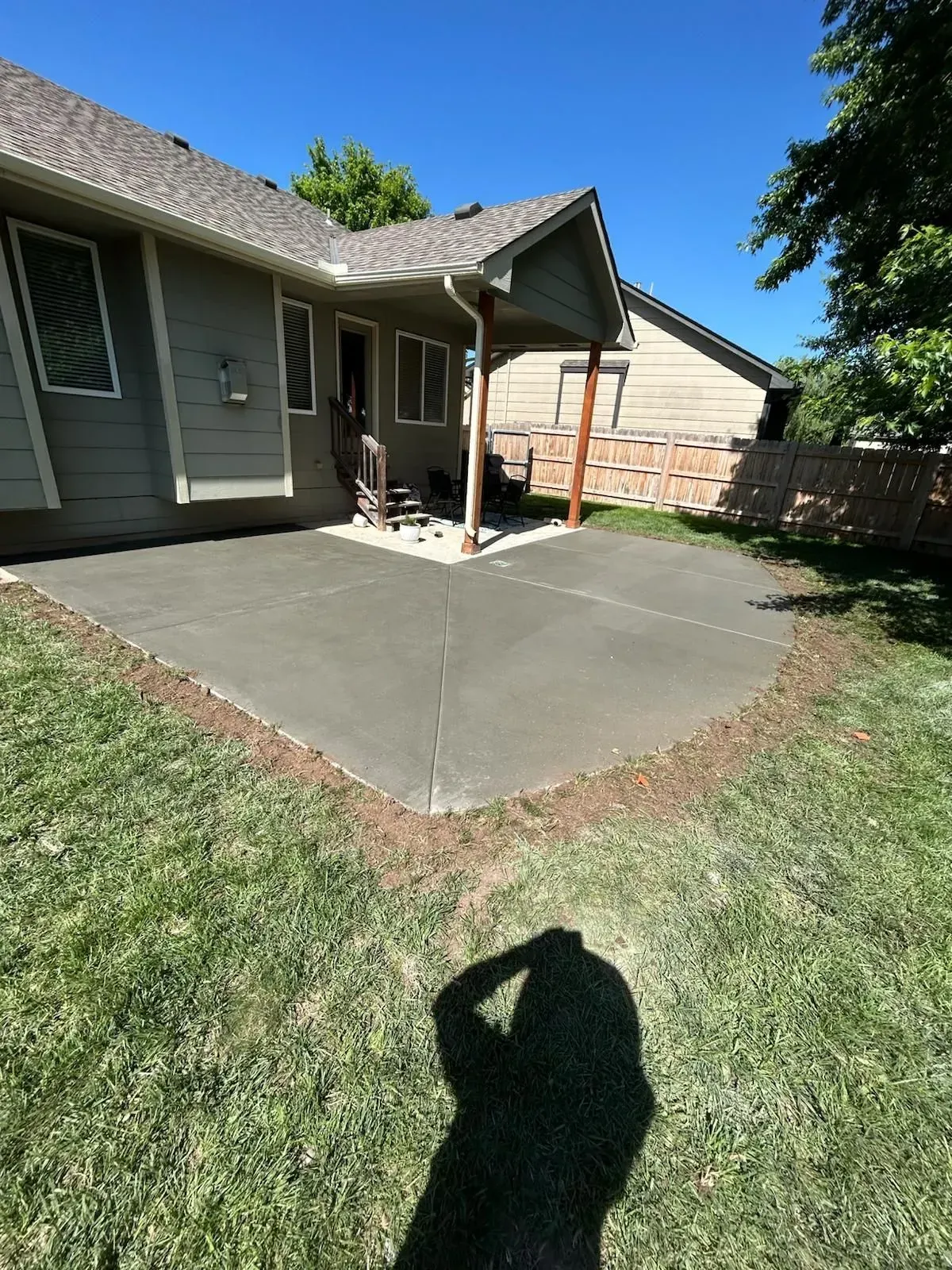 Concrete patio beside a gray house with a covered porch and brick wall, viewed from a grassy yard.