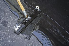 Roof being sealed with black waterproof coating using a squeegee tool