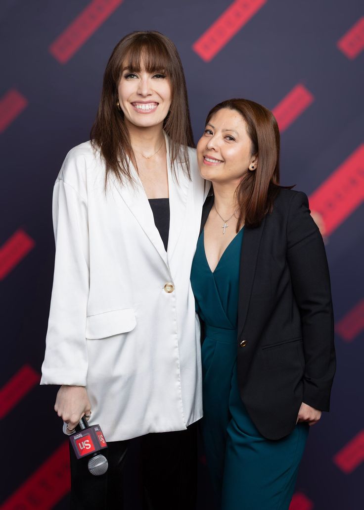 Two people posing together at an event, smiling before a branded backdrop.