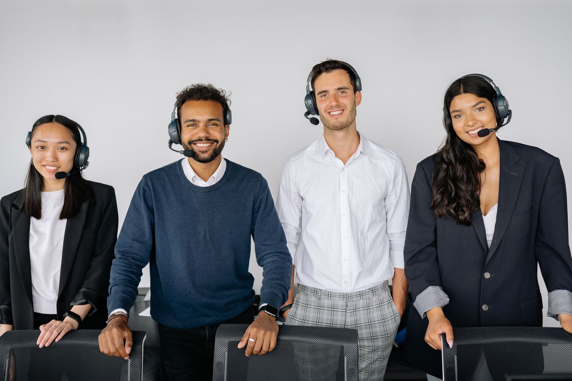 Four coworkers standing and sitting in business-casual clothes, smiling against a plain white background