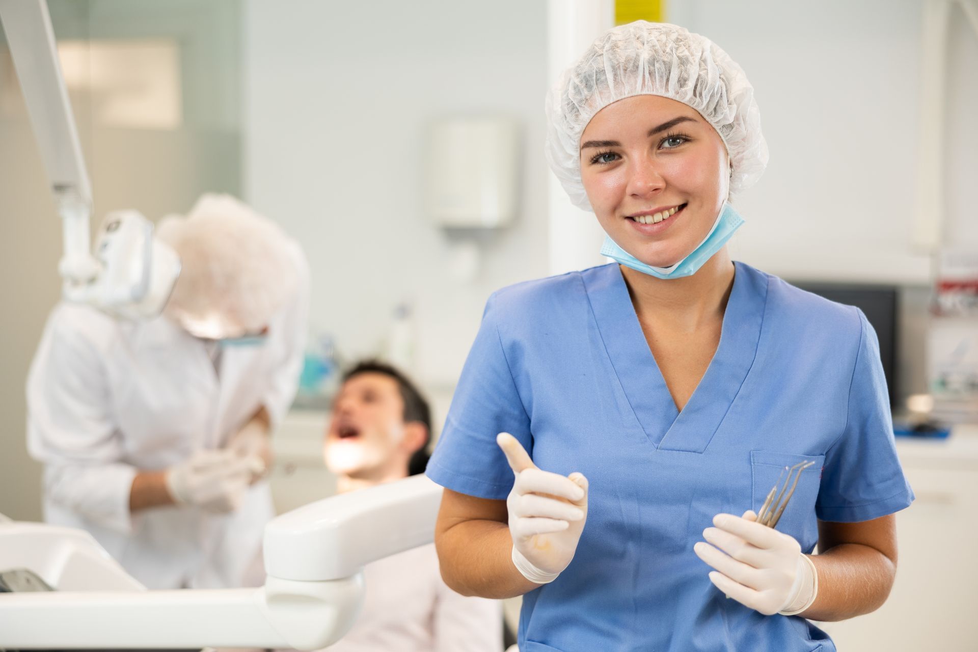 General dentist smiling in blue scrubs holding dental tools in modern clinic setting. General dentist smiling in blue scrubs holding dental tools in modern clinic setting.
