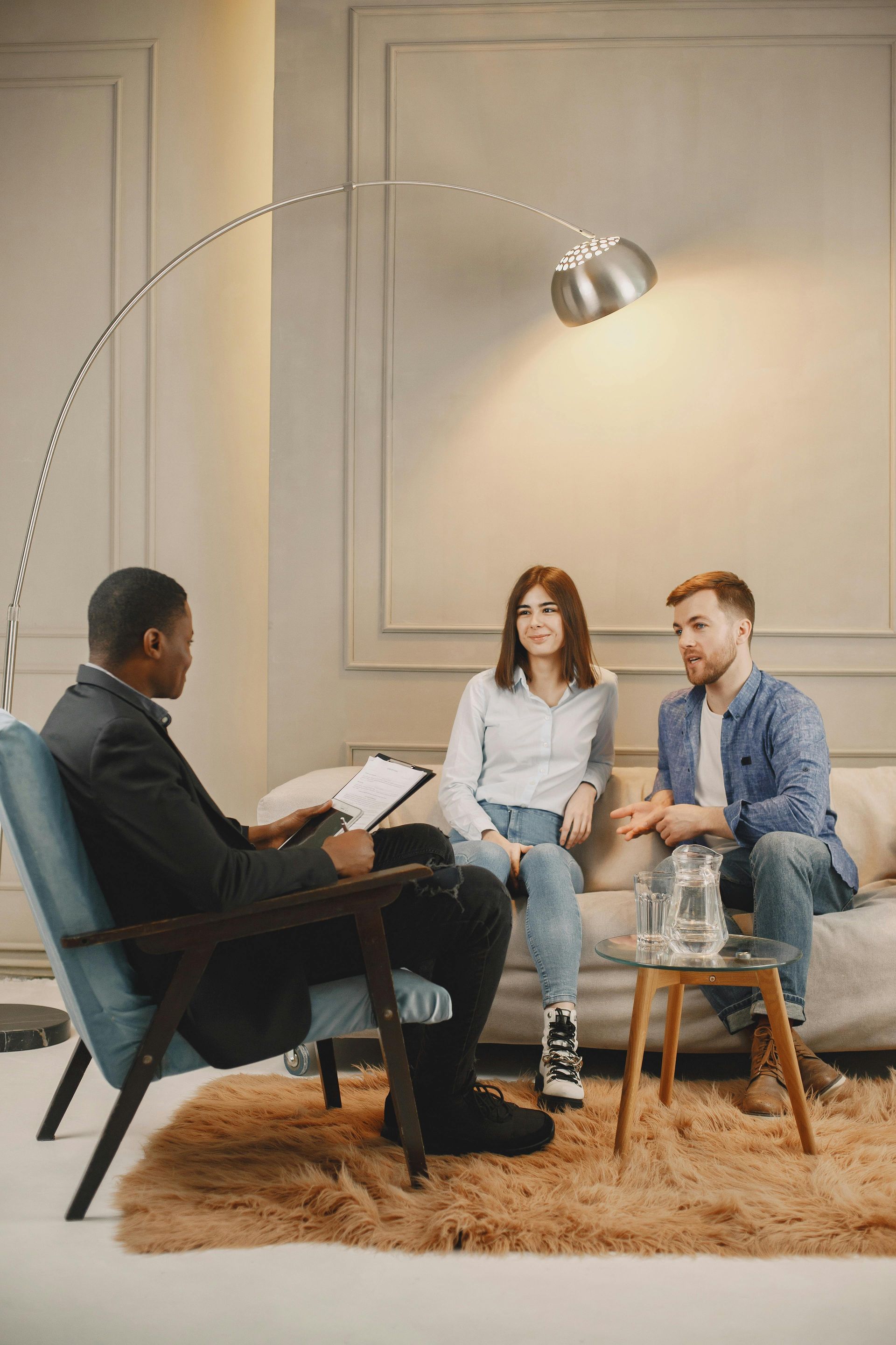 A professional sits in an armchair across from a couple on a sofa in a modern office, conducting a session.