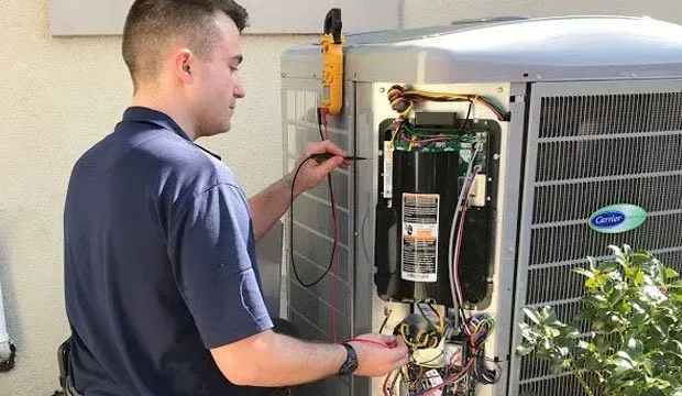 A man is working on an air conditioner with a voltmeter.