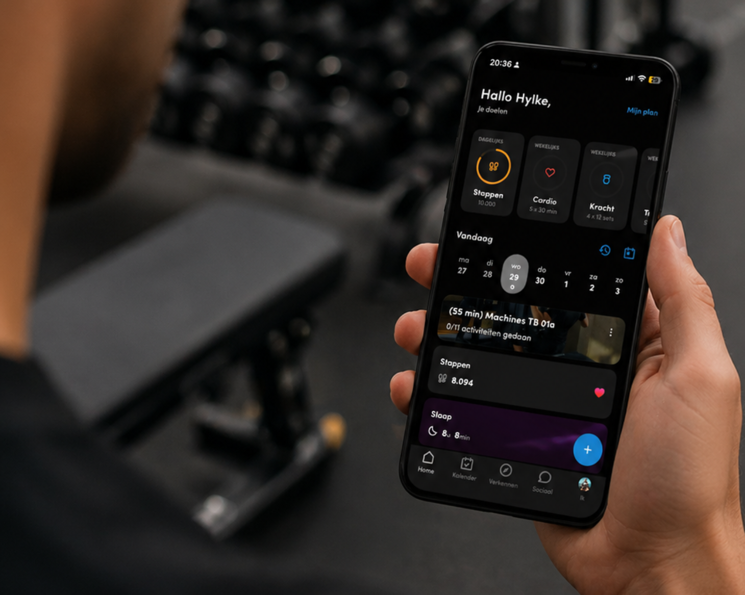 Persoon die een smartphone vasthoudt met een fitness-app in een donker thema, in een sportschoolomgeving.