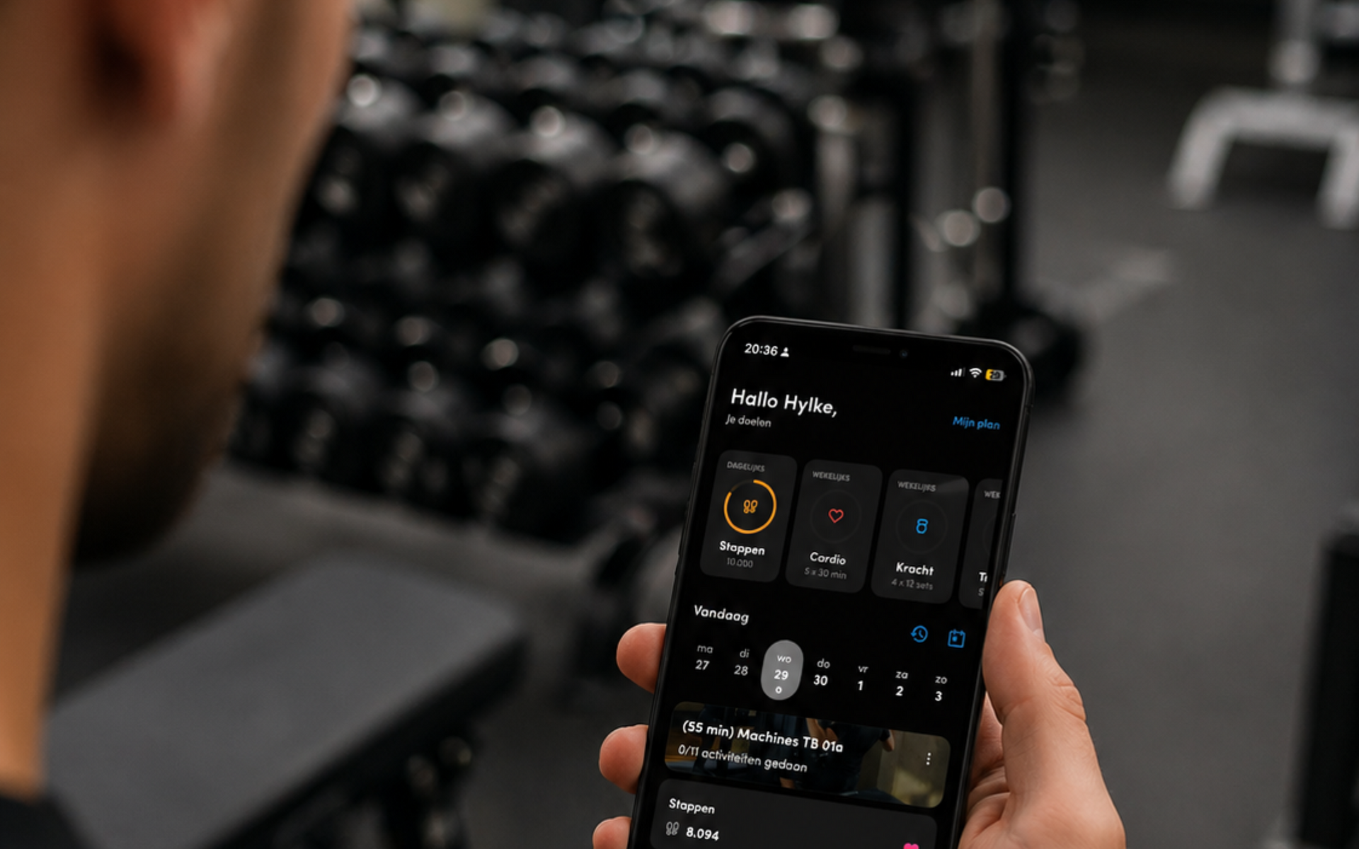 Een persoon met een smartphone waarop een fitness-app openstaat, in een sportschool.