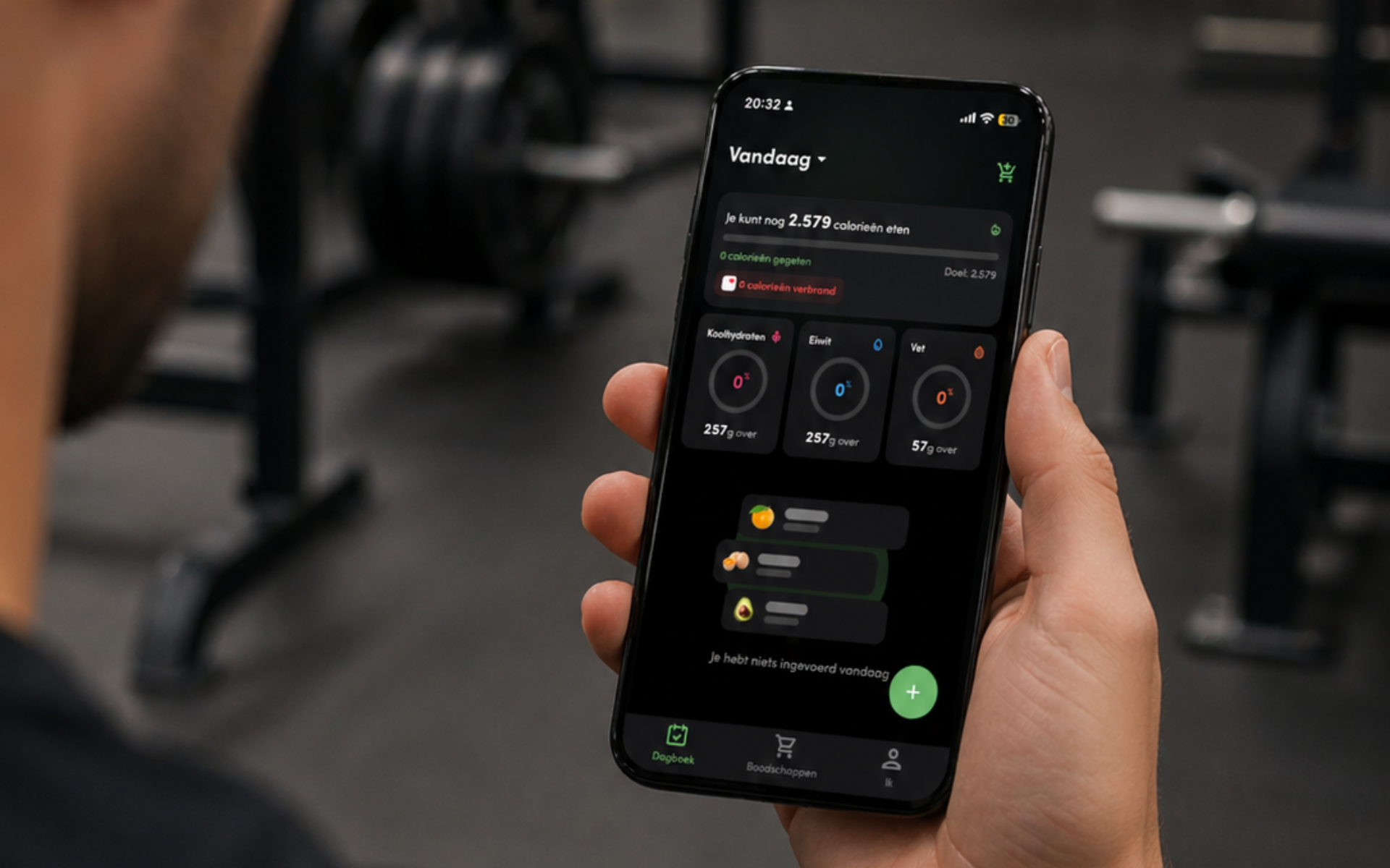 Hand die een smartphone vasthoudt waarop een fitness-app te zien is, in een sportschool met gewichten op de achtergrond.