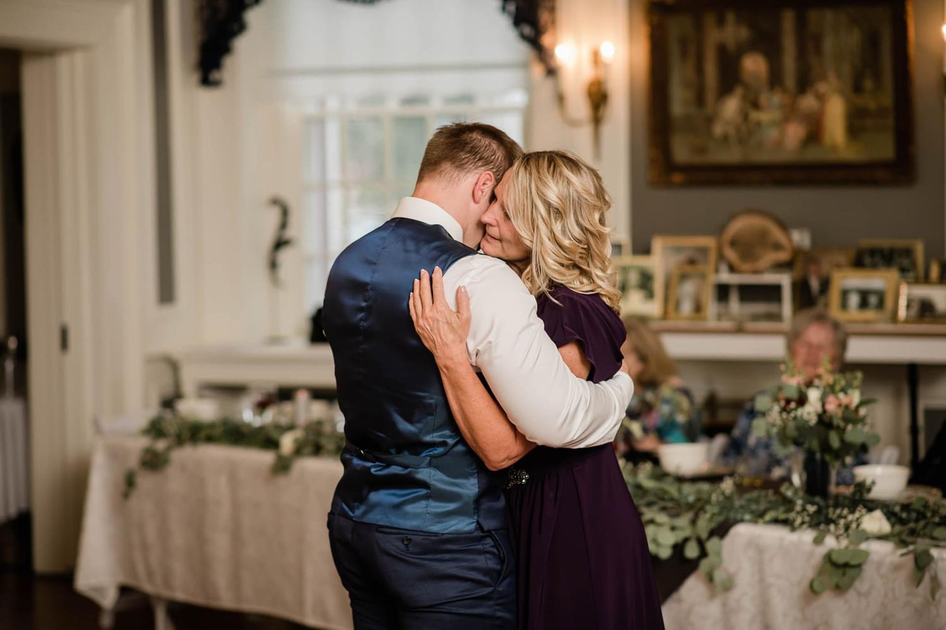 A bride and groom are dancing with their mother at their wedding reception.