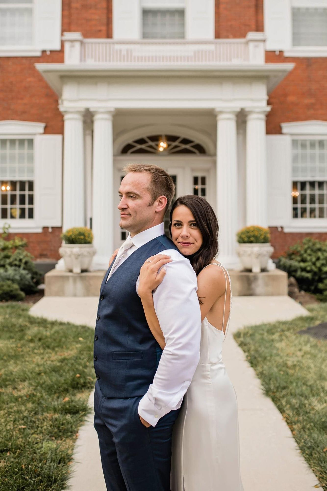 A bride and groom are posing for a picture in front of a large brick building.