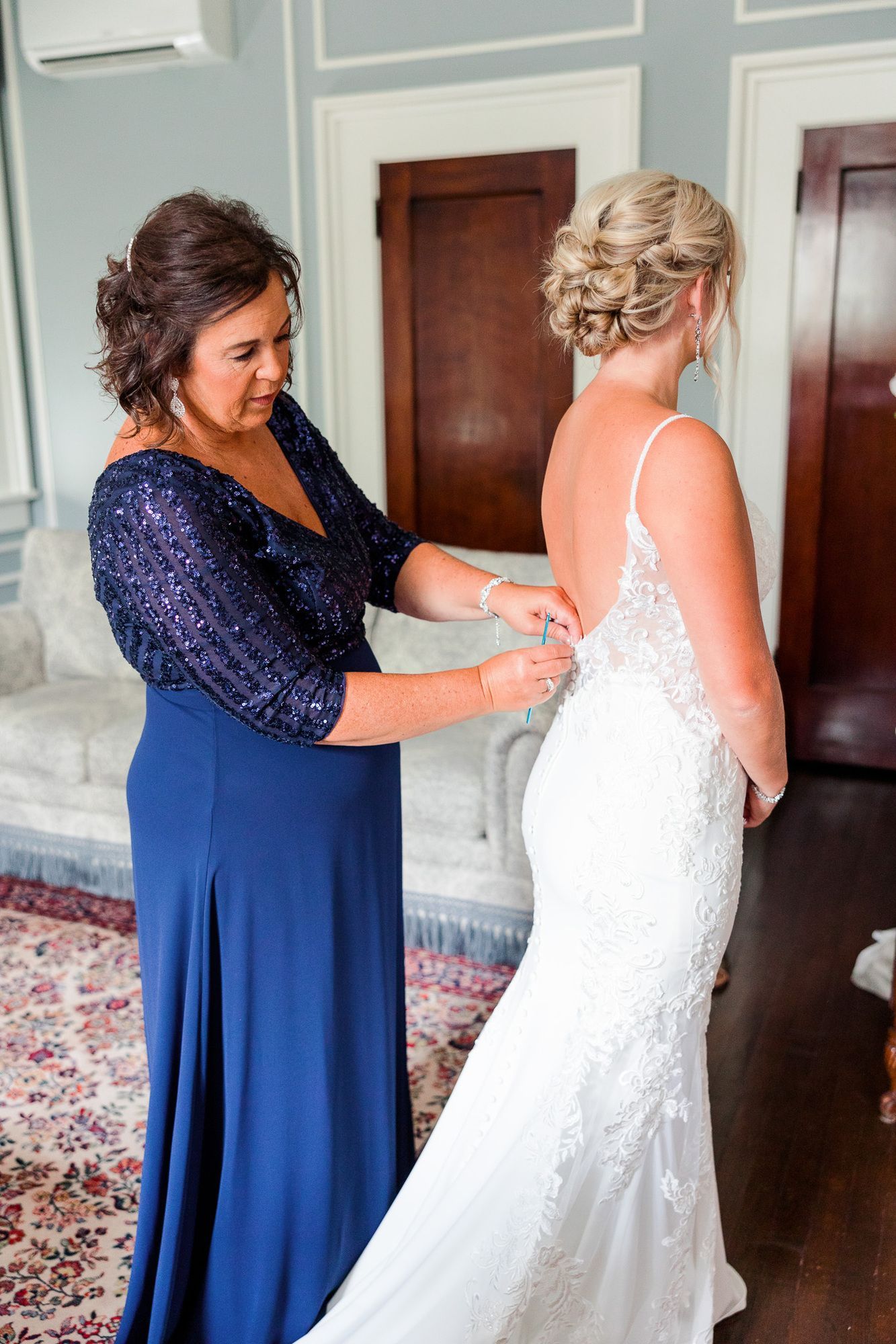 A woman in a blue dress is helping a bride get ready for her wedding.