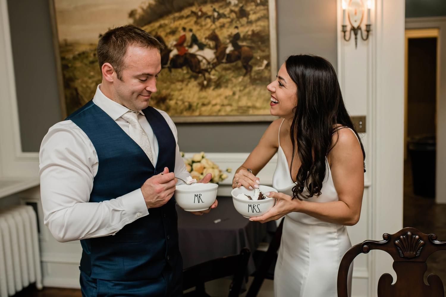 A bride and groom are sitting at a table holding bowls of food.