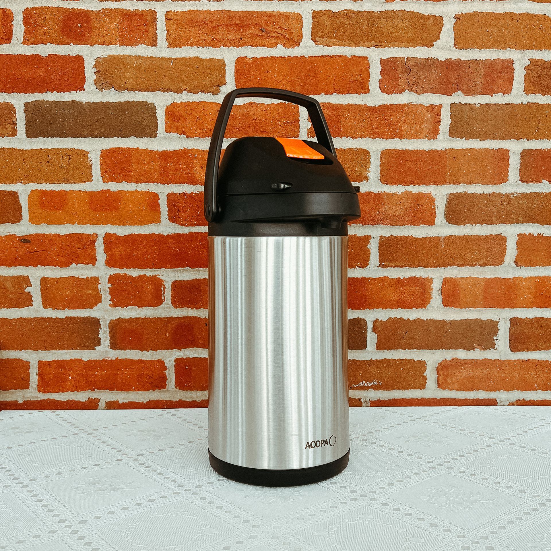 A stainless steel thermos is sitting in front of a brick wall