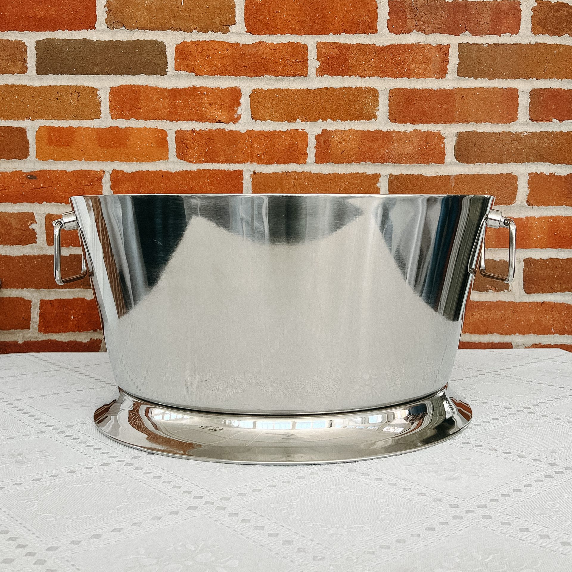 A stainless steel bucket is sitting on a table in front of a brick wall