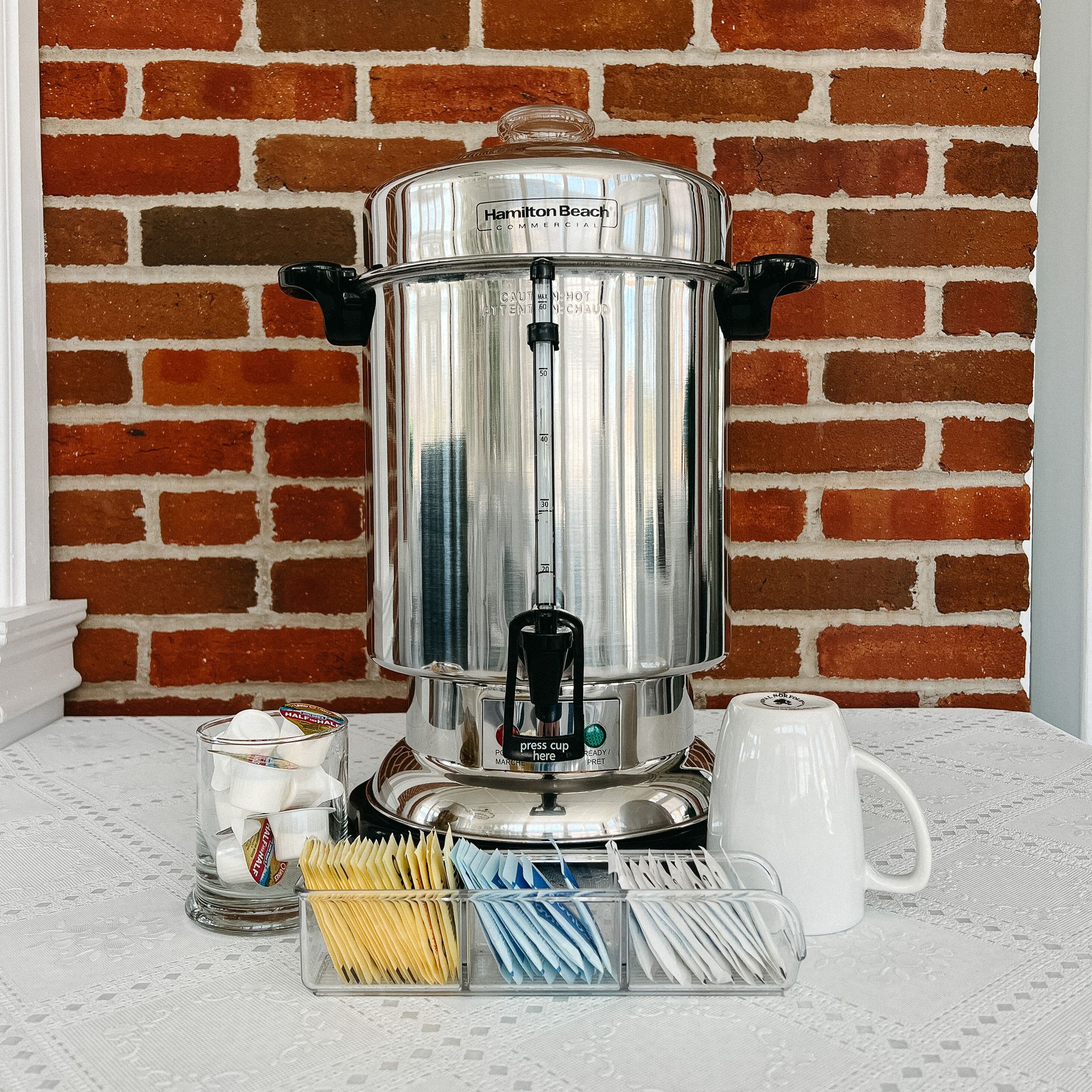A stainless steel coffee percolator with a brick wall in the background