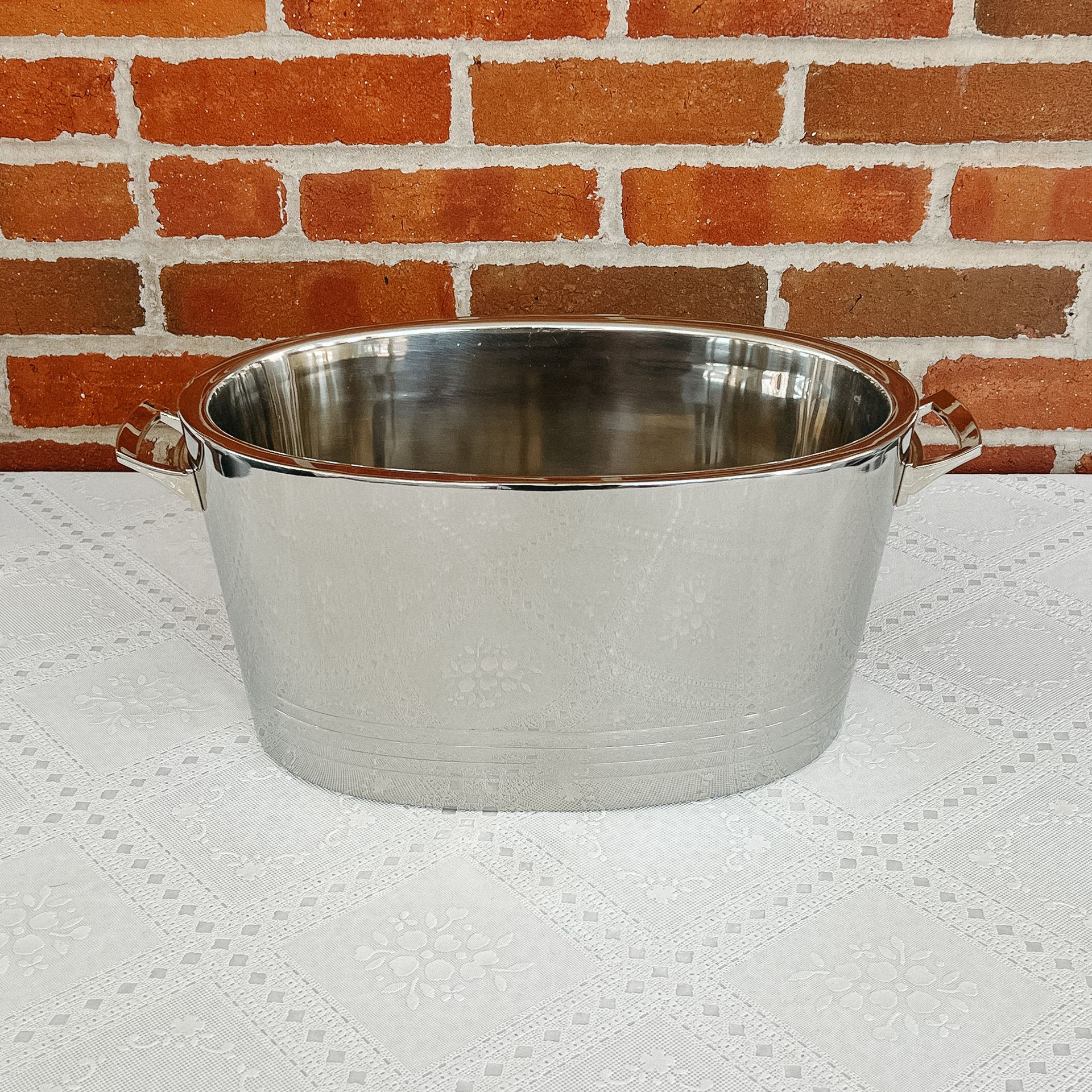 A silver bowl is sitting on a table in front of a brick wall