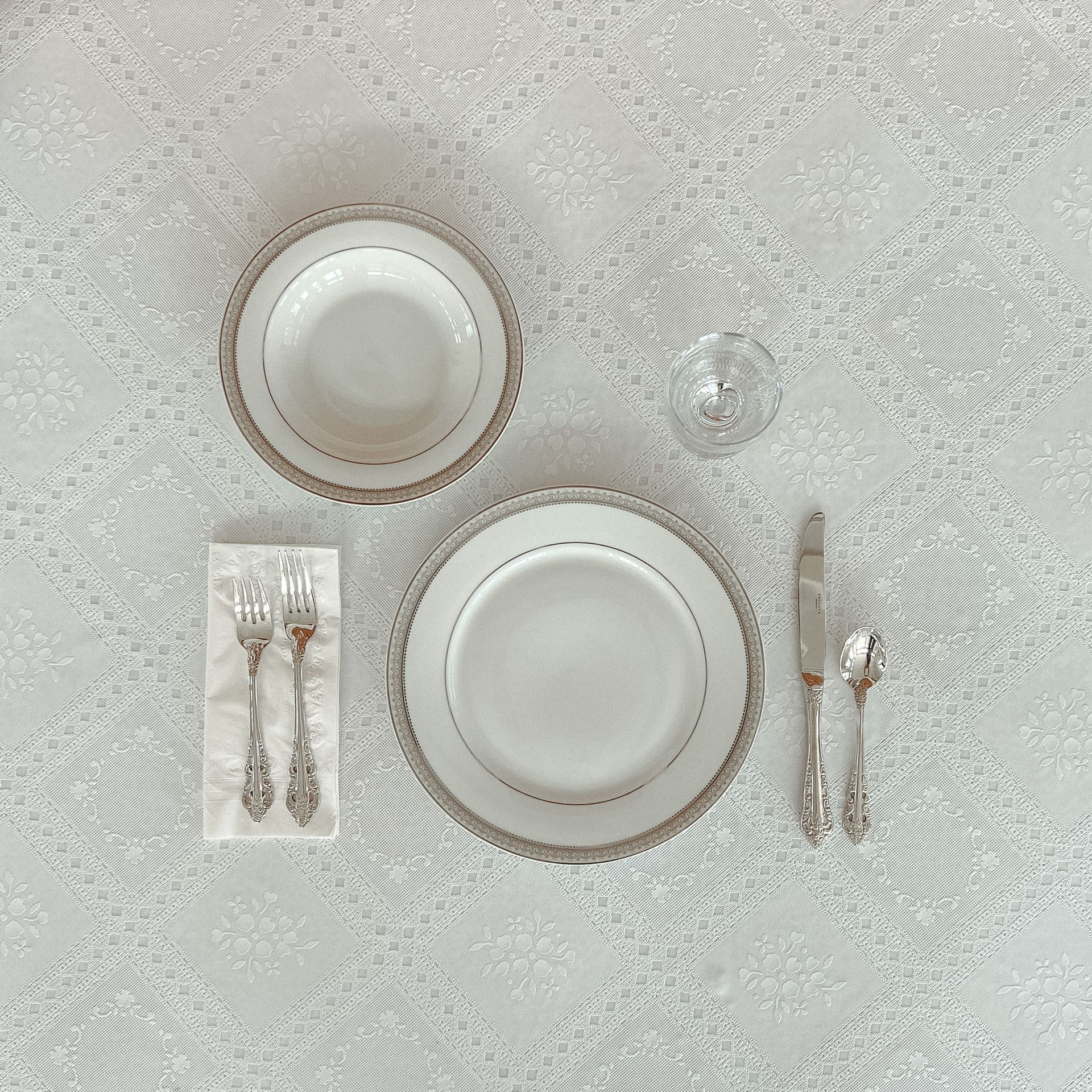 A table setting with plates , bowls , silverware and a napkin.