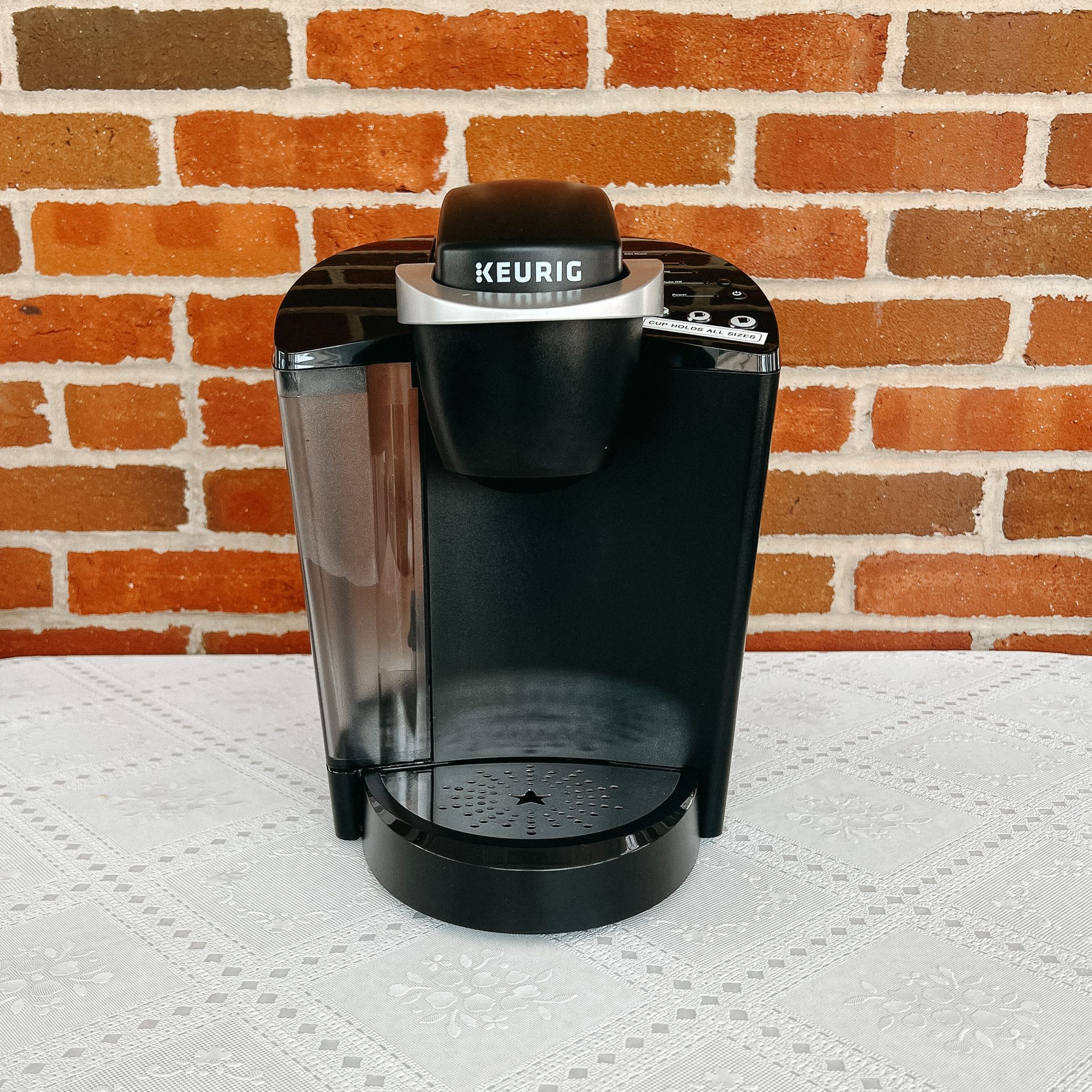 A keurig coffee maker is sitting on a table in front of a brick wall