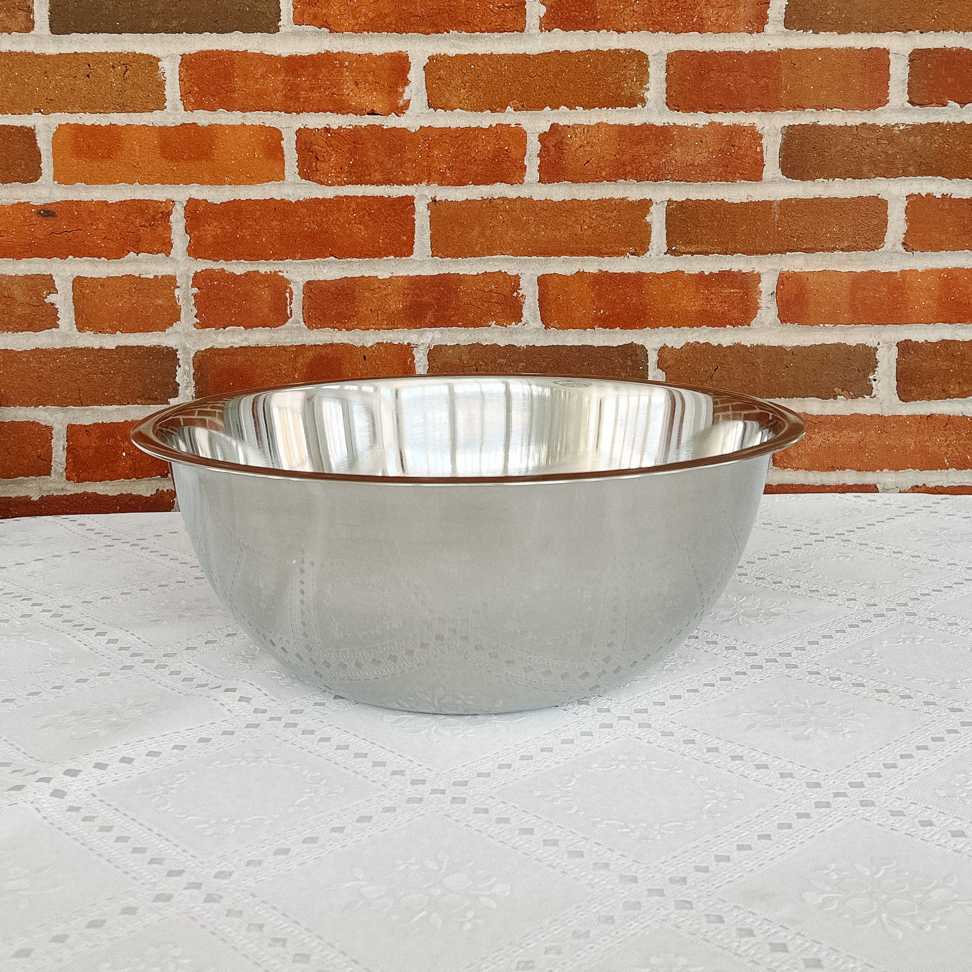 A stainless steel bowl is sitting on a table in front of a brick wall