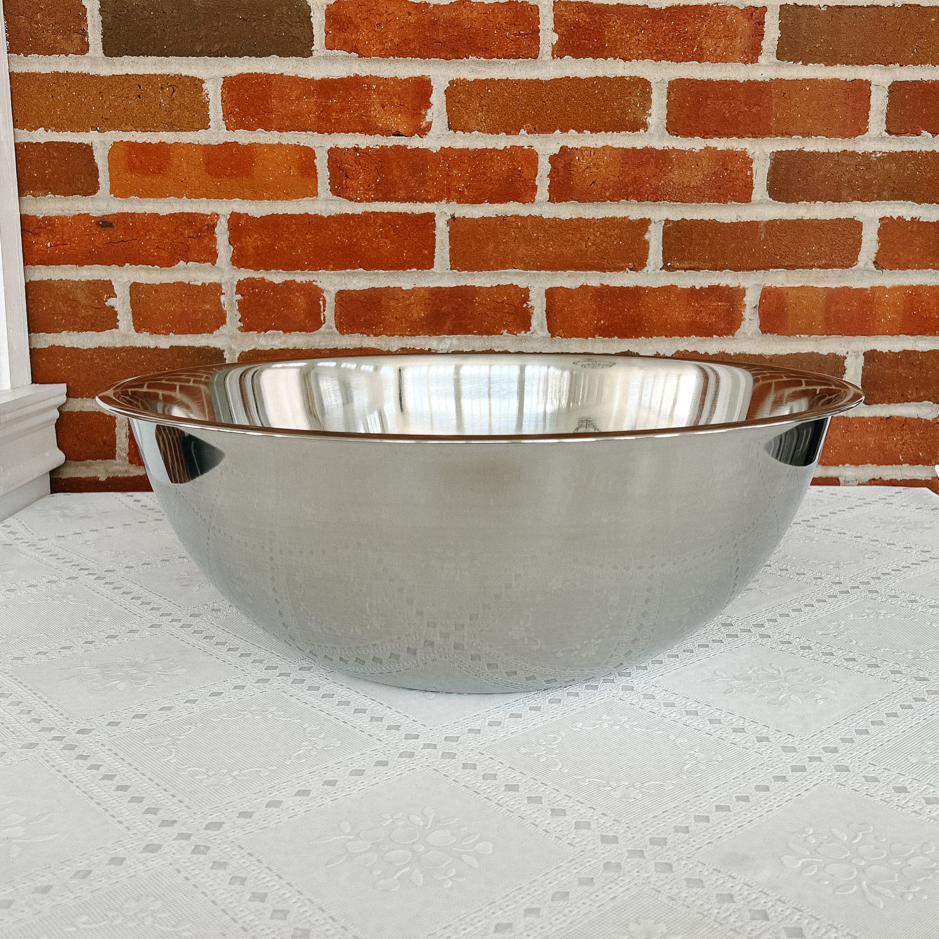 A stainless steel bowl sits on a table in front of a brick wall