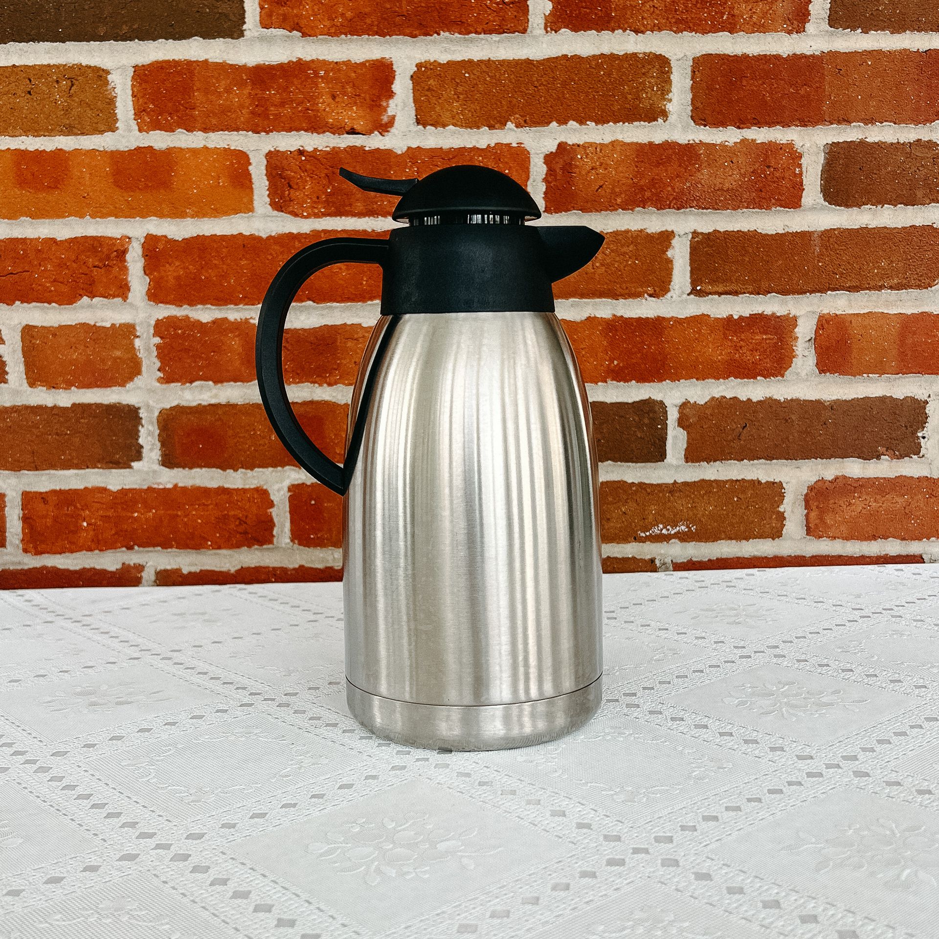 A stainless steel pitcher is sitting on a table in front of a brick wall