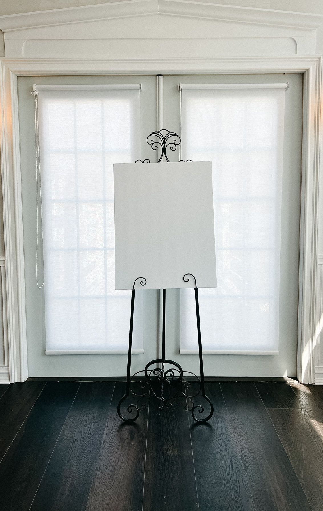A white canvas is sitting on an easel in front of a window.