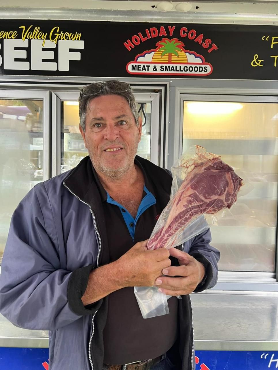 A Man Is Holding a Large Piece of Meat in Front of A Refrigerator — Holiday Coast Meat & Smallgoods in South Grafton, NSW