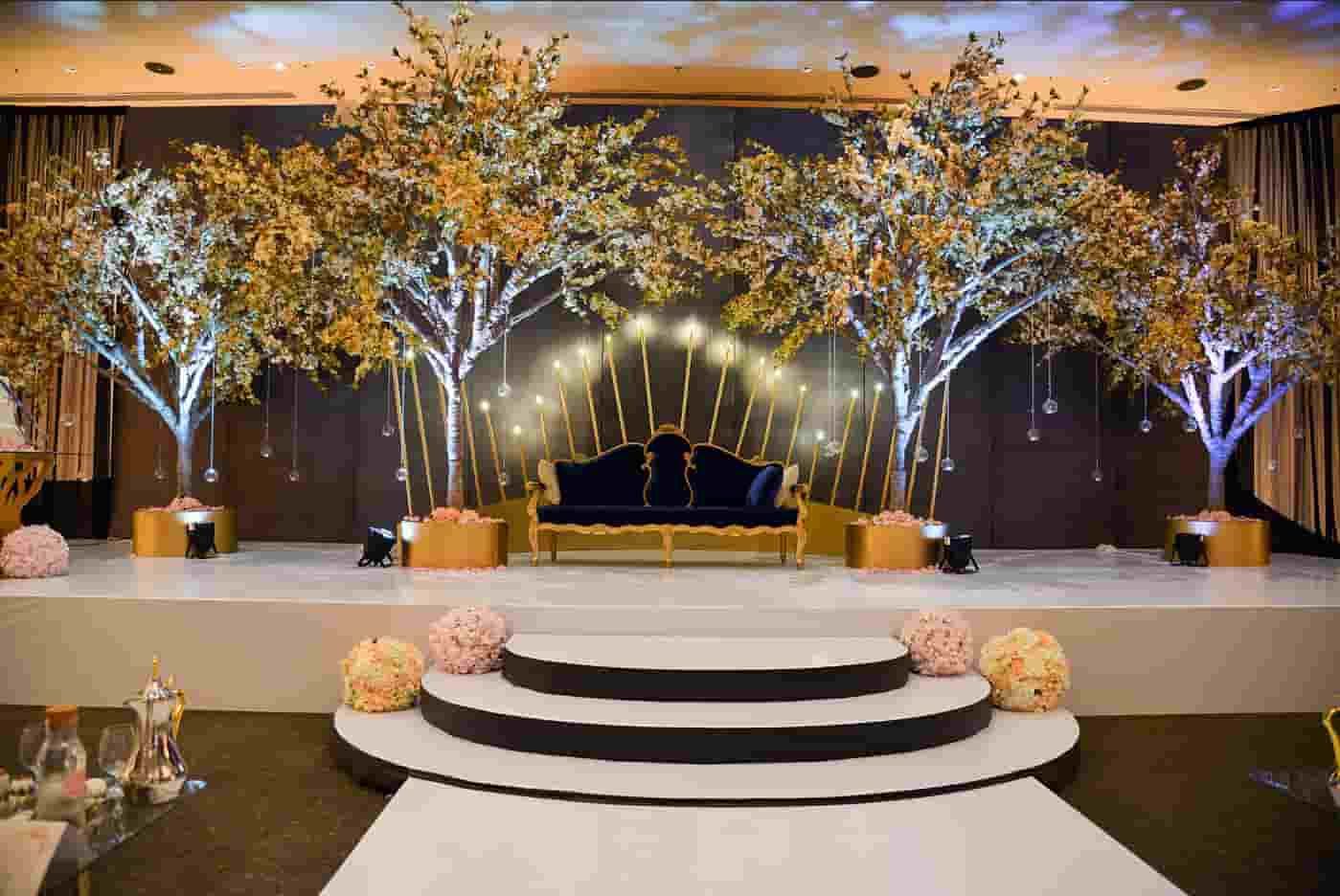 Wedding stage with trees, a blue couch, and string lights.