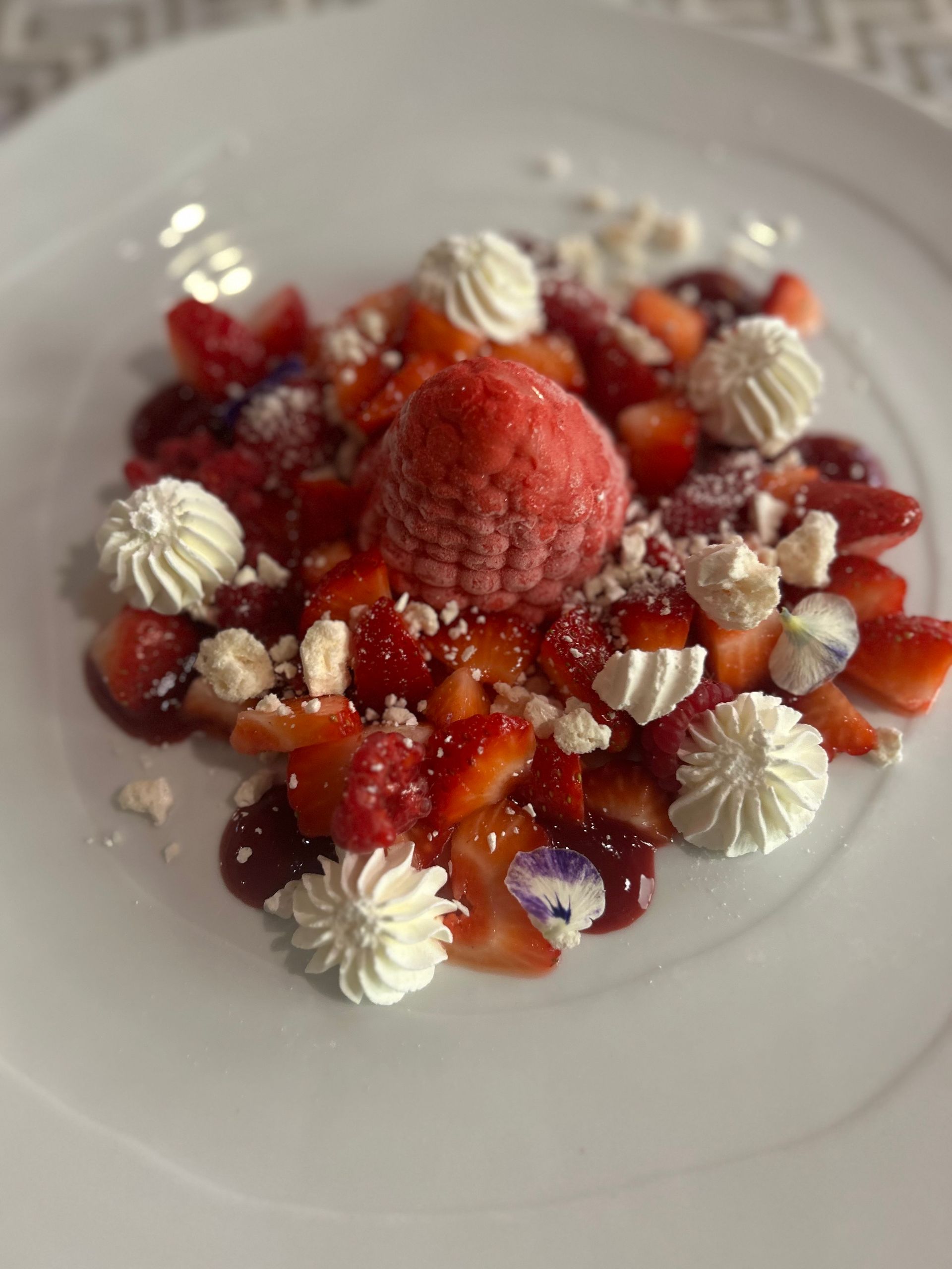 Piatto da dessert con crostata di frutti di bosco guarnita con fragole fresche, ciuffi di panna e zucchero a velo.