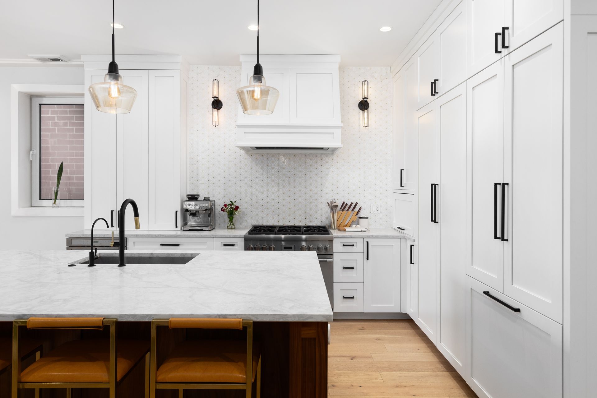 Modern white kitchen with island, marble countertops, pendant lights, and brown accents.