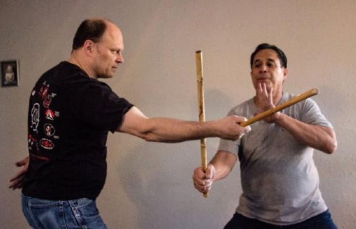Two men are practicing martial arts with sticks in a room.