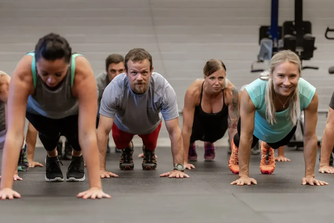 People in fitness class doing push-ups on a black floor.